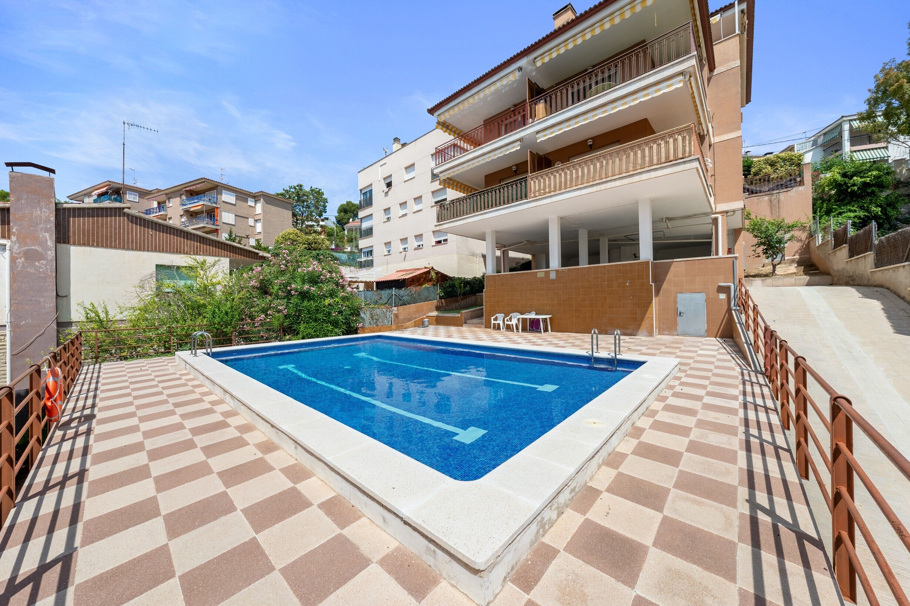 A swimming pool with a checkered floor, surrounded by a fence, and adjacent to a multi-story building with balconies.