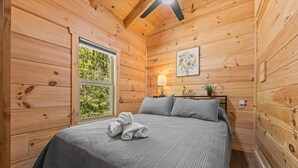 Camera da letto in una baita di legno, con un letto, una finestra, una lampada e un quadro appeso al muro.