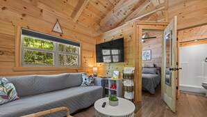 Accogliente interno di una baita con divano, tavolino rotondo, televisore e un letto.