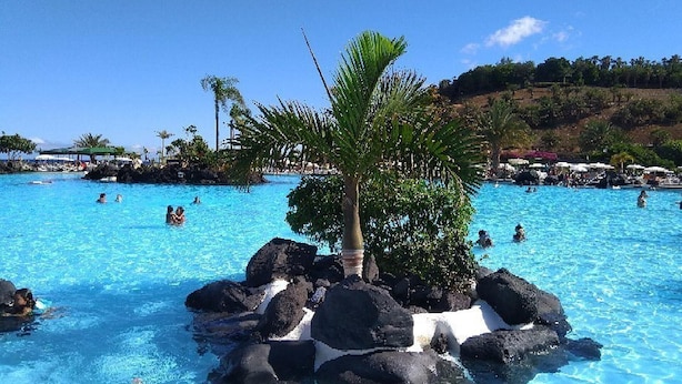 Una piscina con agua azul cristalina, rodeada de rocas y palmeras.
