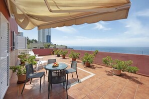 Une terrasse extérieure avec une table et des chaises, des plantes en pot et une vue sur la mer.