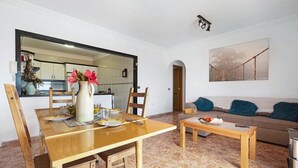 Una sala de estar con una mesa de comedor de madera, un sofá y una mesa de centro. Se ve una cocina a través de un arco.