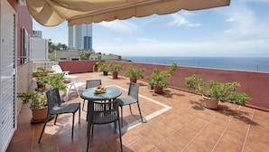 Una terraza con mesa y sillas, plantas en macetas y vista al mar.
