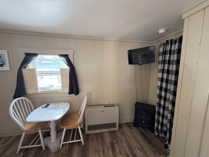 A small room with a table and two chairs, a heater, a television mounted on the wall, and a window with curtains.