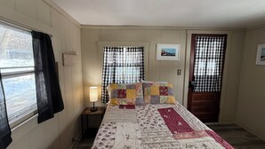 Ein Schlafzimmer mit einem Bett, zwei Fenstern mit Karomustervorhängen, einer Nachttischlampe und einem gerahmten Bild an der Wand.