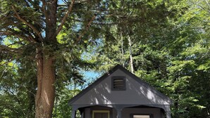 Eine kleine Holzhütte mit Veranda, Treppe und Tür, umgeben von Bäumen.