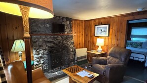 Una sala de estar acogedora con chimenea de piedra, un sillón de cuero y una mesa de centro de madera con un tablero de ajedrez.