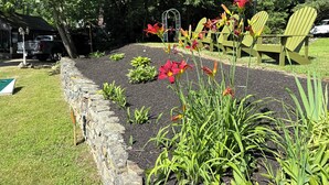 Un jardín con muro de piedra, césped verde y valla de madera.