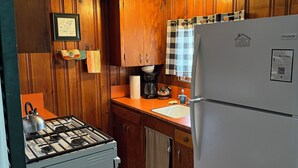 Una cocina compacta con armarios de madera, una estufa a gas, un refrigerador y un lavamanos.