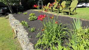 Ein Garten mit einer Steinmauer, blühenden Pflanzen und grünen Stühlen.
