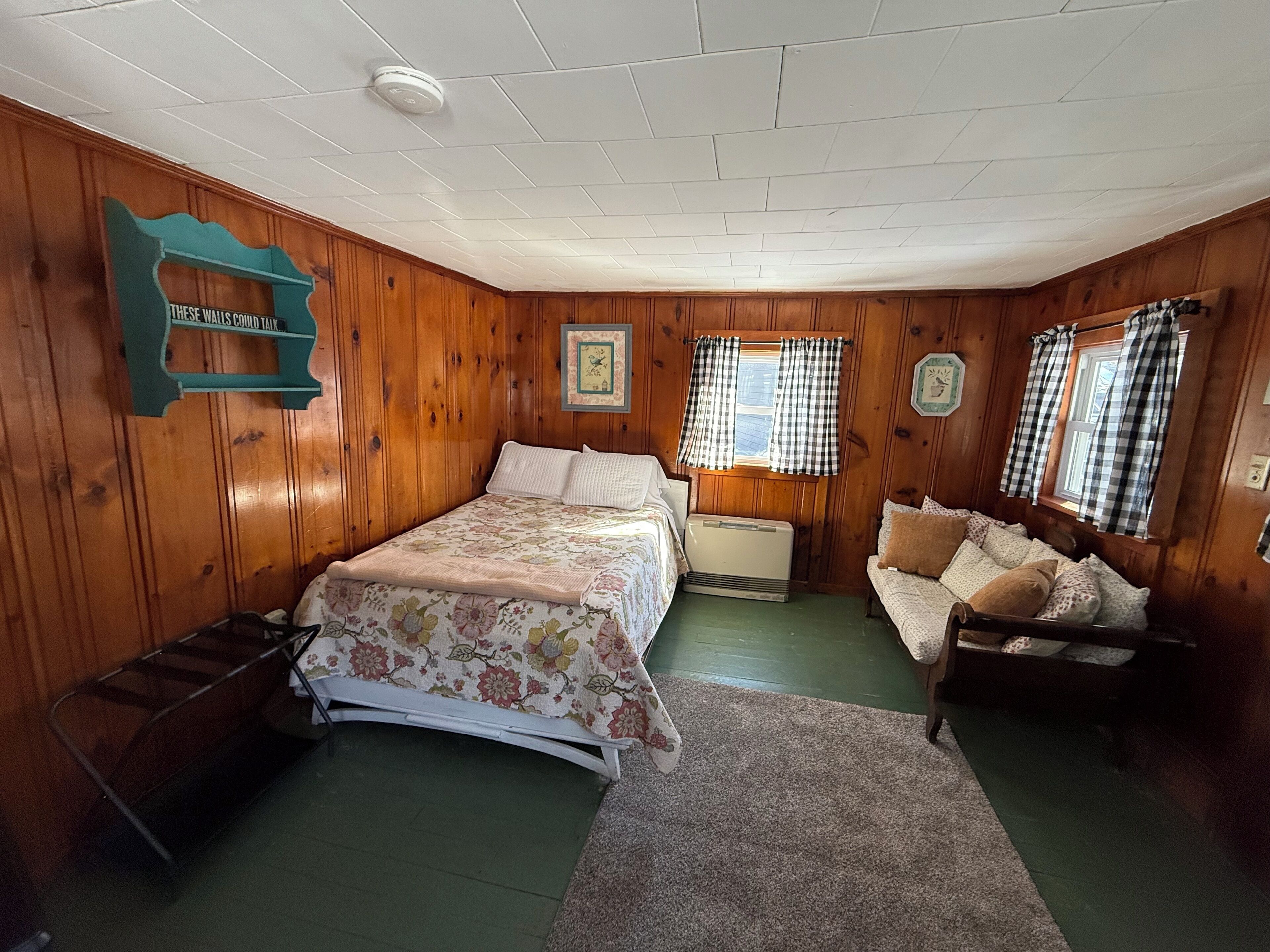 A bedroom with a bed, a nightstand, a chair, a radiator, and a window with curtains.