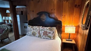 A bedroom with a wooden headboard, a bed with floral bedding, a bedside lamp, and a small wooden nightstand. - Lakeside Cabin 6 with Kitchen (Holderness)