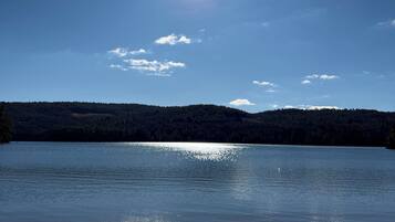 A clear view of a lake with a sandy beach in the foreground and a forested hill in the background.