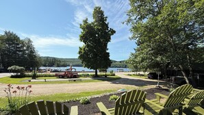 Un espacio exterior con asientos tipo Adirondack, un sendero de grava y vistas a un lago con barcos.