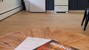 Una cocina con un refrigerador blanco, estufa y microondas. Hay una mesa de madera con una revista y un menú.