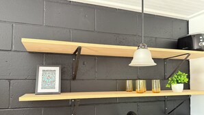 Et køkken med træhylder, en hængende lampe, et indrammet billede, en plante og en vanddispenser.
