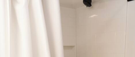 A shower with a black handle, a white curtain, and a tiled wall.