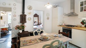 Een keuken met een kookplaat, oven en kasten. Er is een eettafel met stoelen en een bloemenvaas.