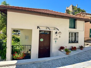 Um edifício com telhado de azulejos, porta de madeira e uma pequena varanda com plantas em vasos.