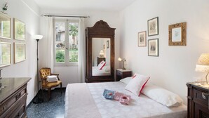 Een slaapkamer met een bed, een stoel, een dressoir, een spiegel en foto's in lijsten aan de muur.