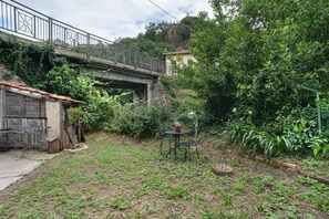 A rustic outdoor area with a wooden table and chairs, a metal bench, and a small garden. - Apartment 'Al Frantoio' with Private Garden (Castelvecchio di Rocca Barbena)