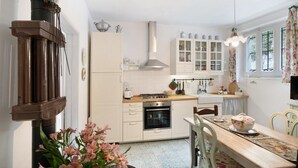 Een keuken met witte kastjes, een fornuis, oven en een eettafel met stoelen.