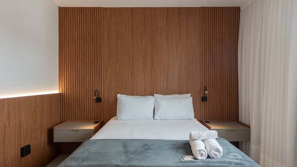 A hotel room with a wooden headboard, a bed with white linens, two bedside tables, and a blue throw blanket. - MHFs Apartamentos com Vista Mar Itapema (Itapema)