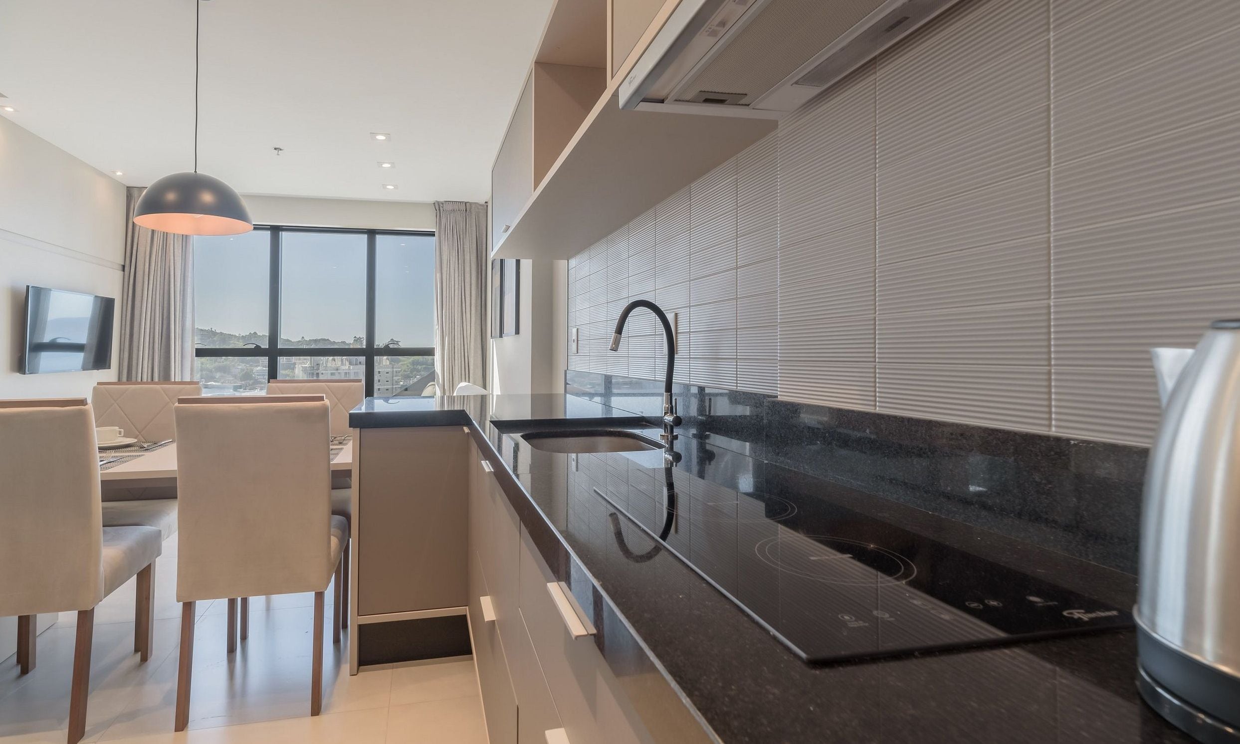 Una cocina moderna con encimera negra, electrodomésticos de acero inoxidable y un amplio ventanal con vistas a la ciudad.