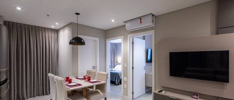 A modern hotel room with a dining area, a TV, and an air conditioning unit.