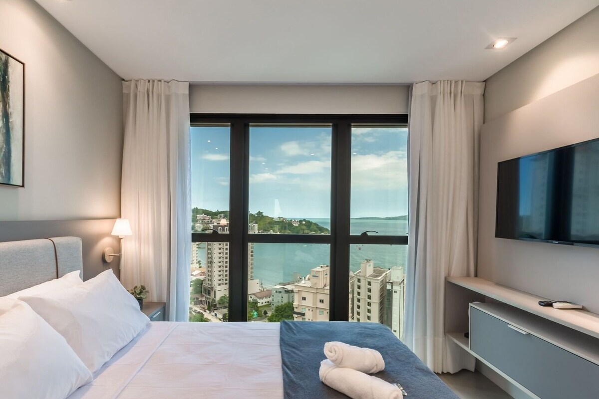 Une chambre d’hôtel avec un lit, une télévision, une fenêtre donnant sur la ville et un tableau accroché au mur.