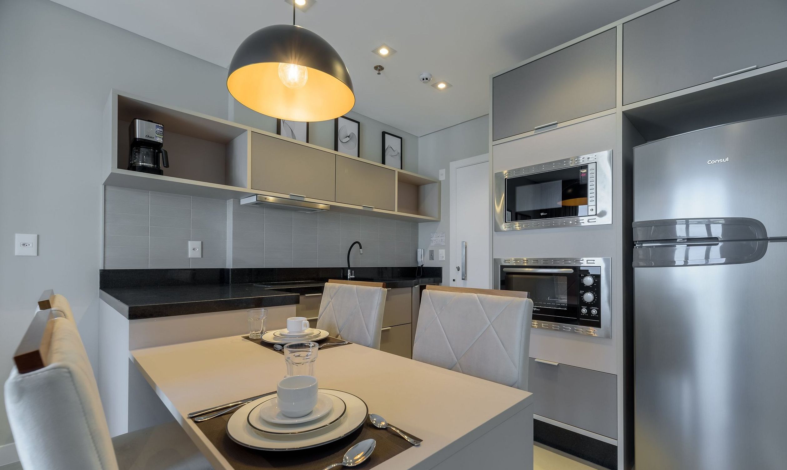 A modern kitchen with built-in appliances, a dining area with a table set for two, and a pendant light above.