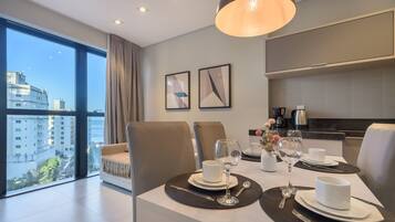 A modern dining area with a table set for two, a sofa, and a view of the cityscape.