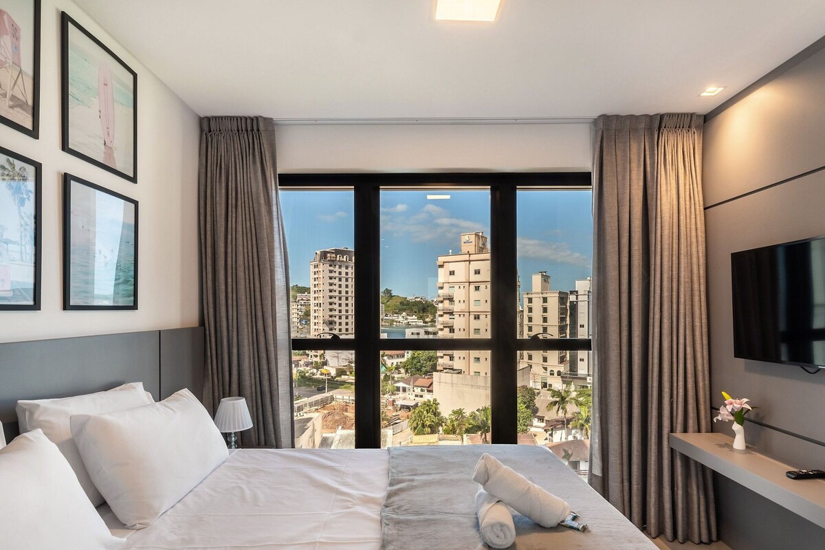 Une chambre d’hôtel avec un lit, une télévision, une fenêtre avec des rideaux et des tableaux encadrés au mur.