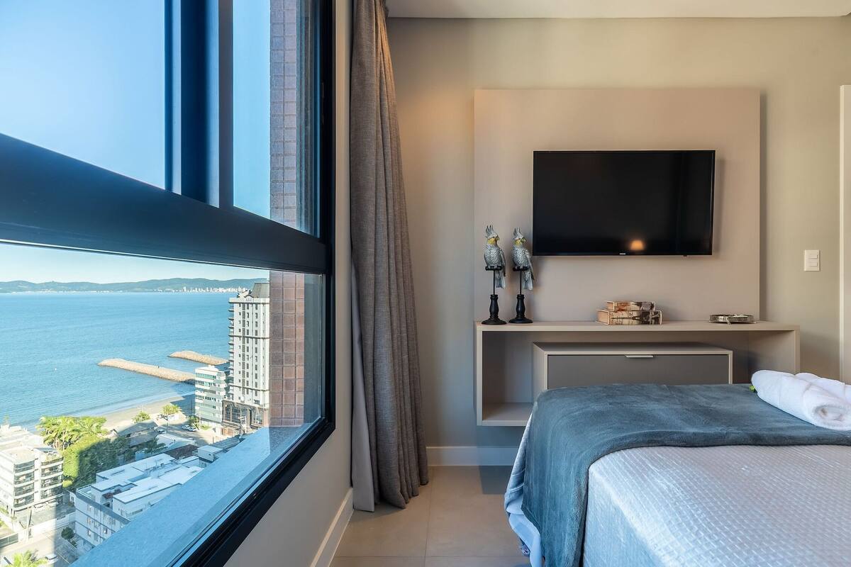A hotel room with a large window, a bed, a TV, and a small console table.