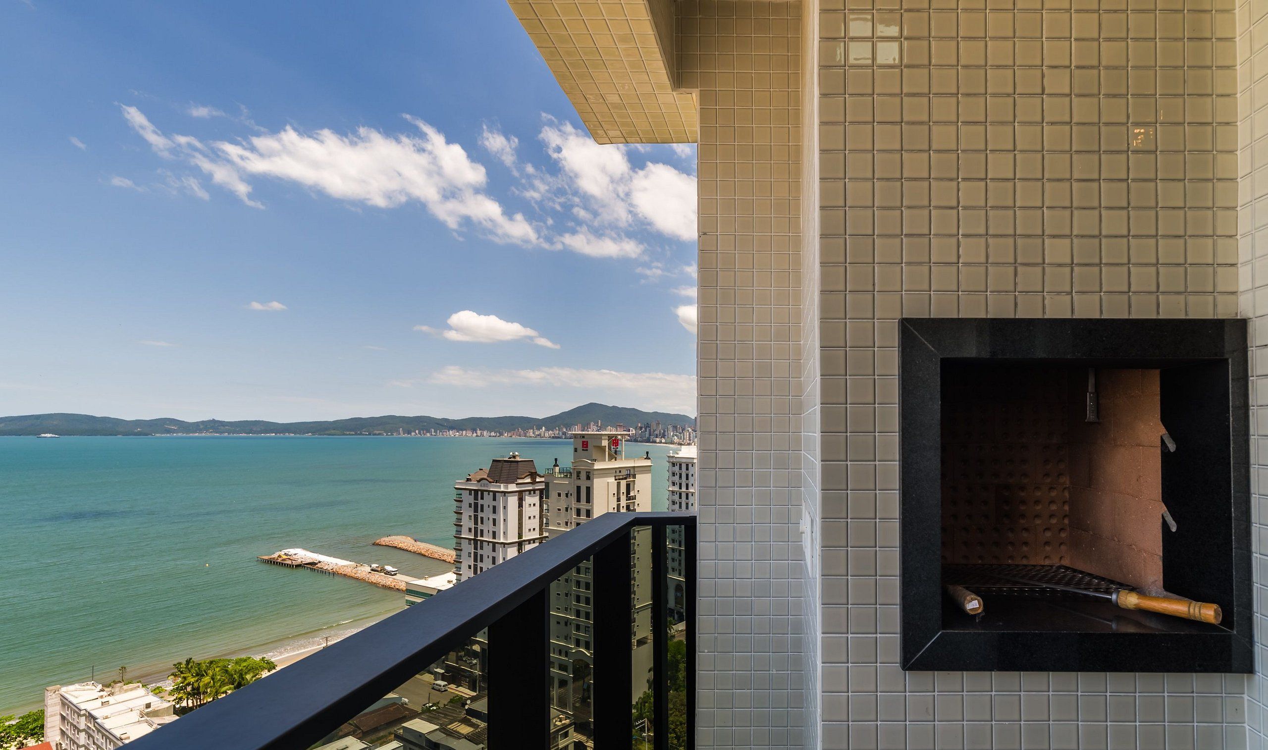 A balcony with a view of the sea and a cityscape, a tiled wall, and a fireplace with a chimney.
