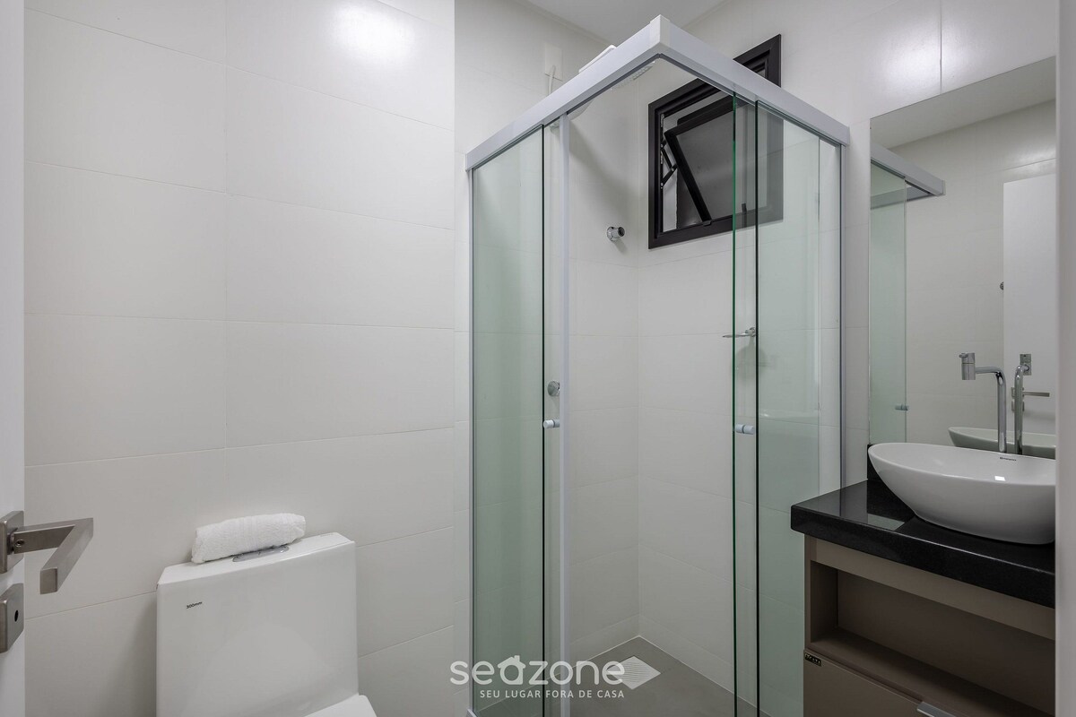 Un baño moderno con cabina de ducha de vidrio, inodoro blanco y lavabo con encimera negra.