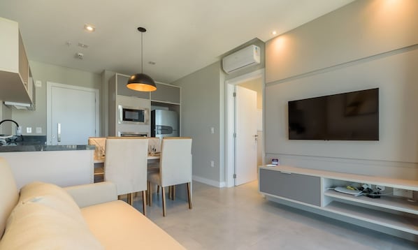 Een moderne woonkamer met een bank, eethoek, keuken en een wandgemonteerde televisie.