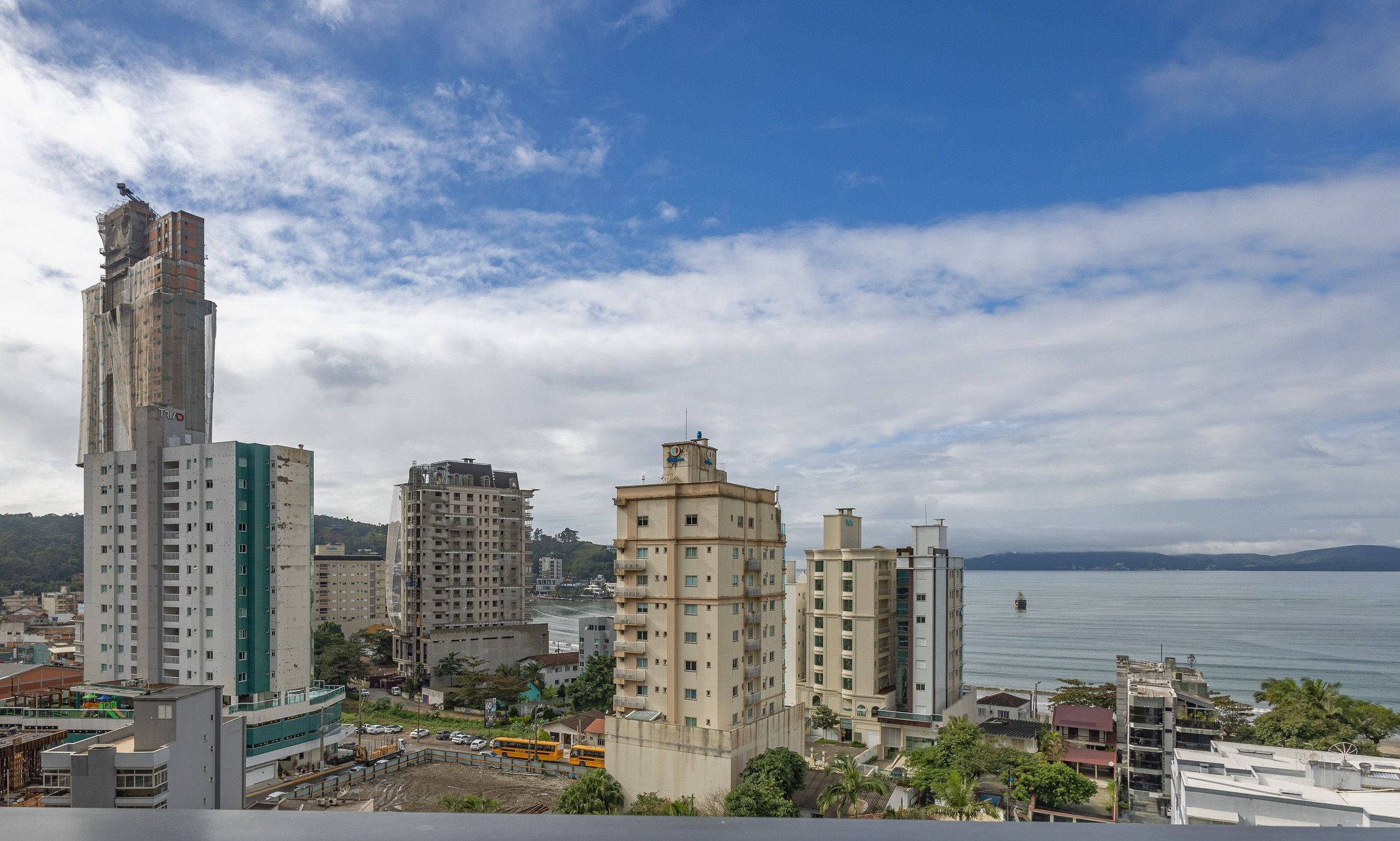 Un paisaje urbano costero con rascacielos, cielo despejado y mar tranquilo.