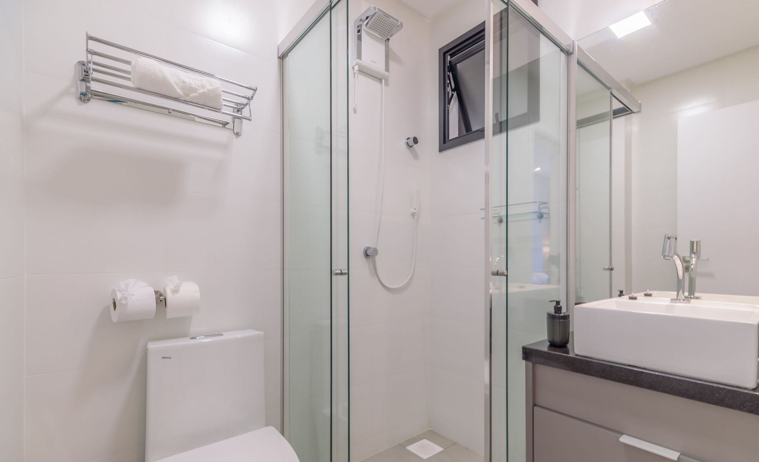 Un baño moderno con cabina de ducha de vidrio, inodoro blanco y lavamanos con espejo.