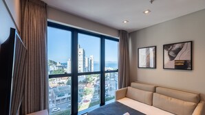 A modern hotel room with a large window, a sofa, and two framed artworks. - MHFs Apartamentos com Vista Mar Itapema (Itapema)