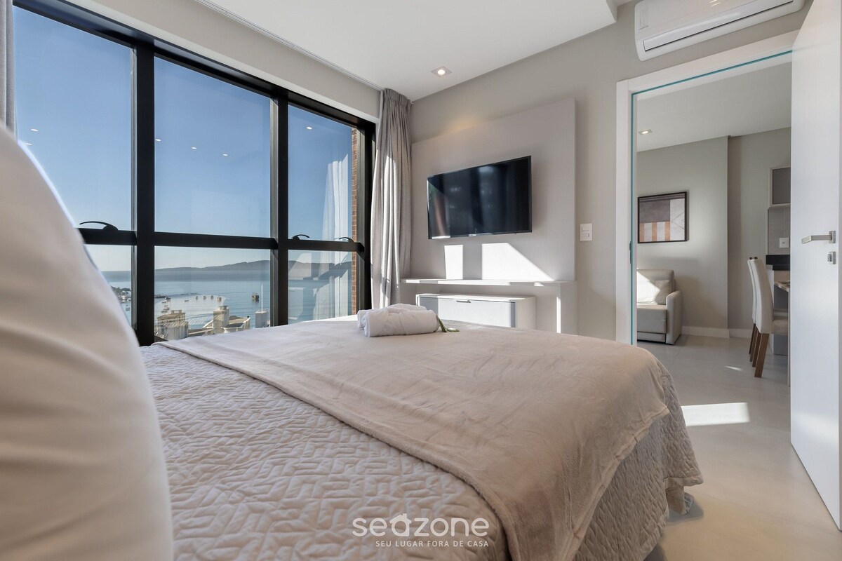 A modern hotel room with a large bed, a TV, and a view of the city.