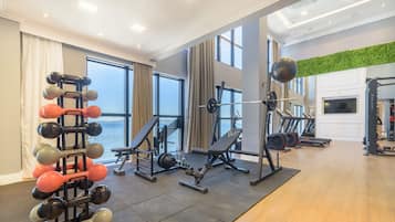 Un gimnasio con diverso equipamiento de ejercicio, amplias ventanas y vista al mar.