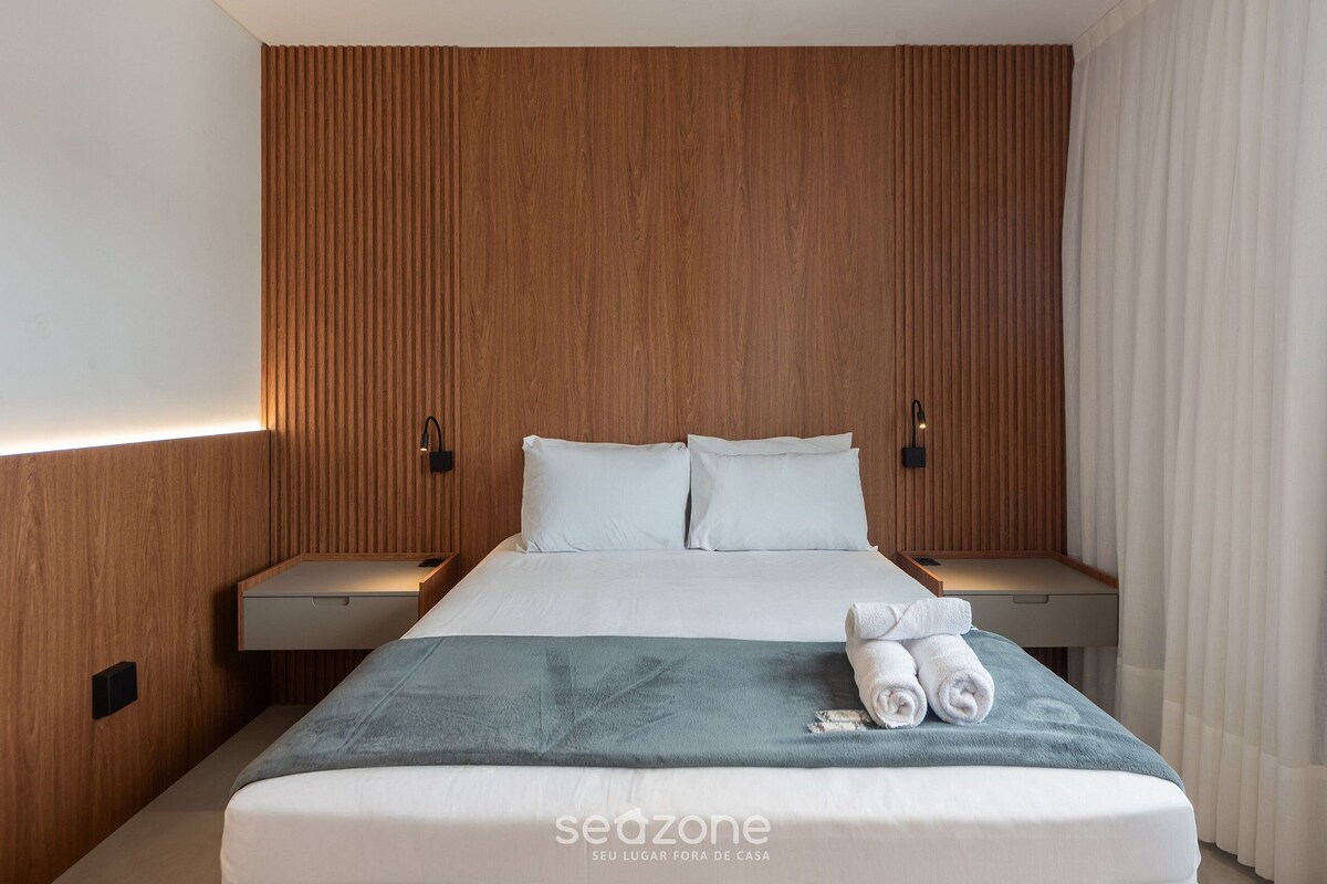 Une chambre d’hôtel avec une tête de lit en bois, un lit recouvert de draps blancs, deux tables de chevet et un plaid bleu.
