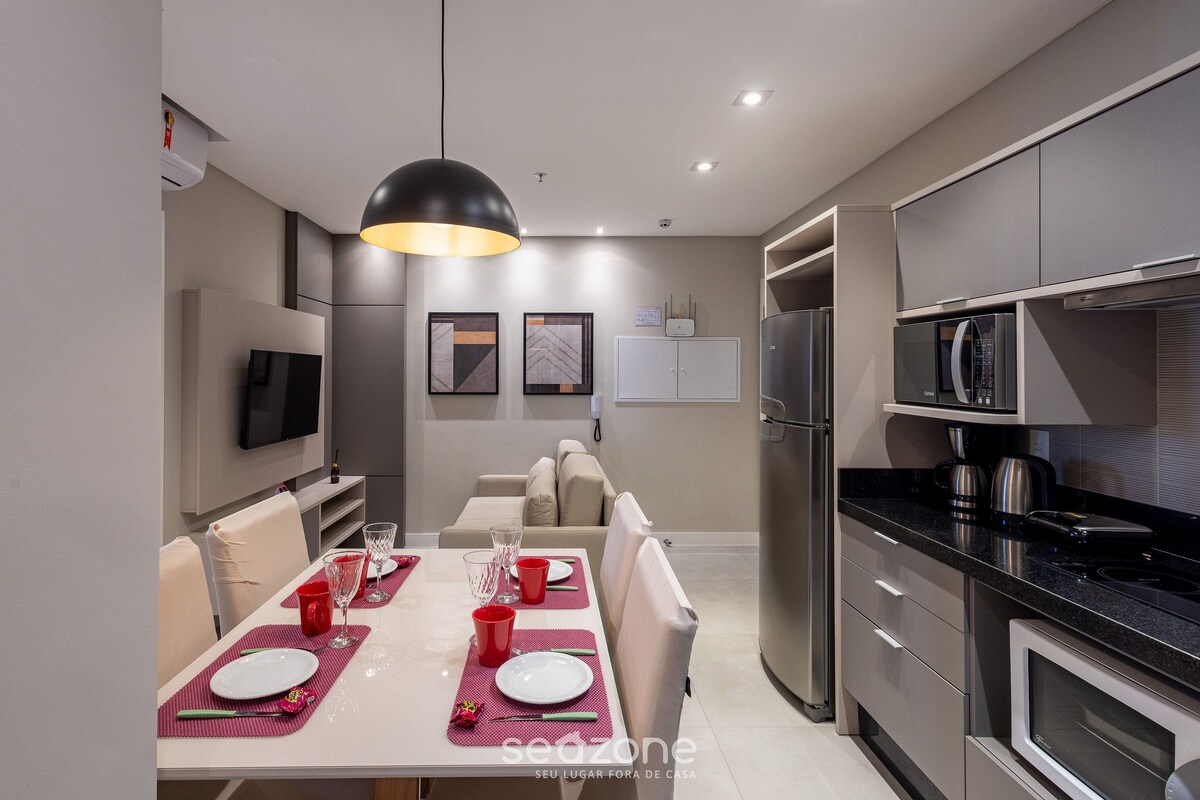 A modern kitchen with stainless steel appliances, a dining area with a table set for two, and a sofa in the background.