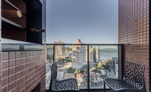 A balcony with two chairs, a view of a cityscape, and a tiled wall. - MHFs Apartamentos com Vista Mar Itapema (Itapema)