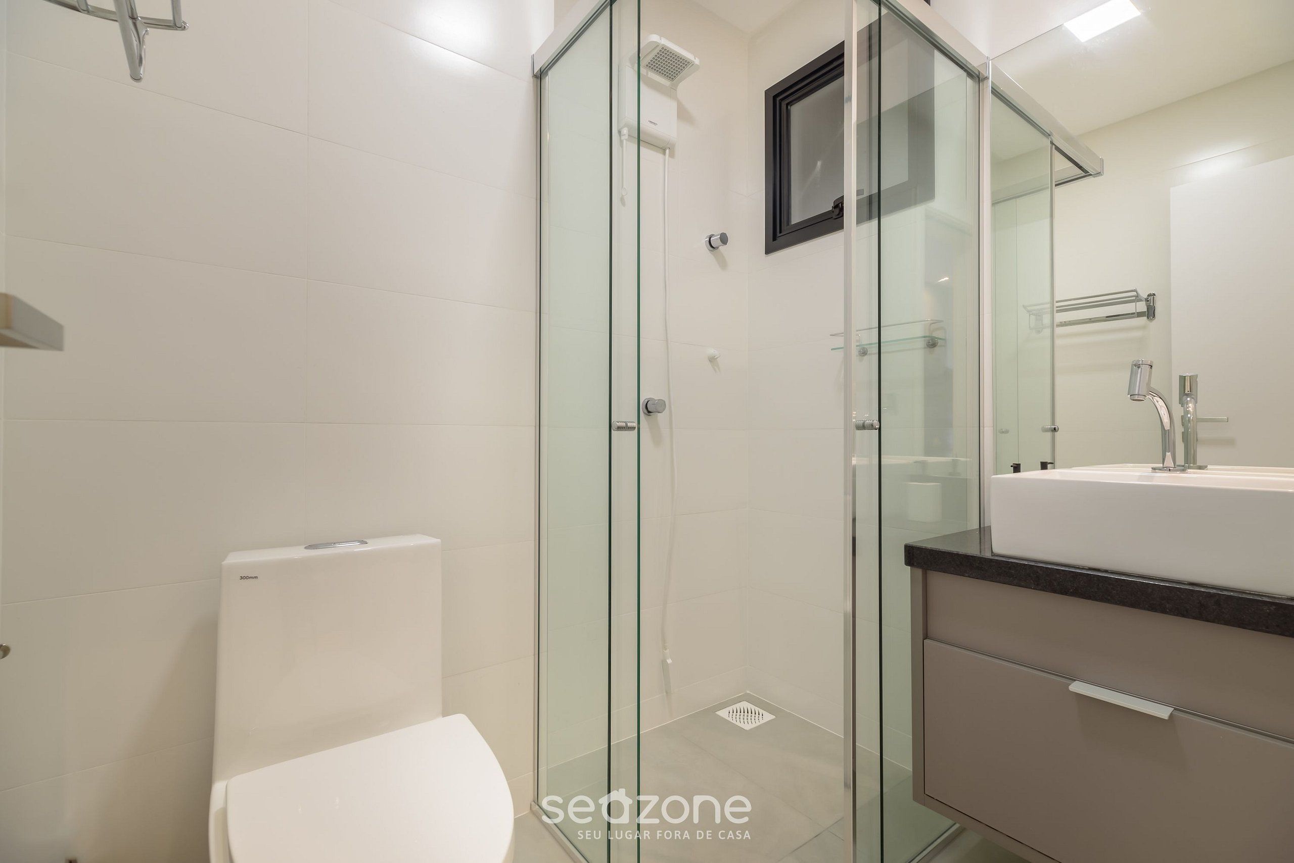 Un baño moderno con cabina de ducha de vidrio, inodoro blanco y lavamanos con encimera negra.