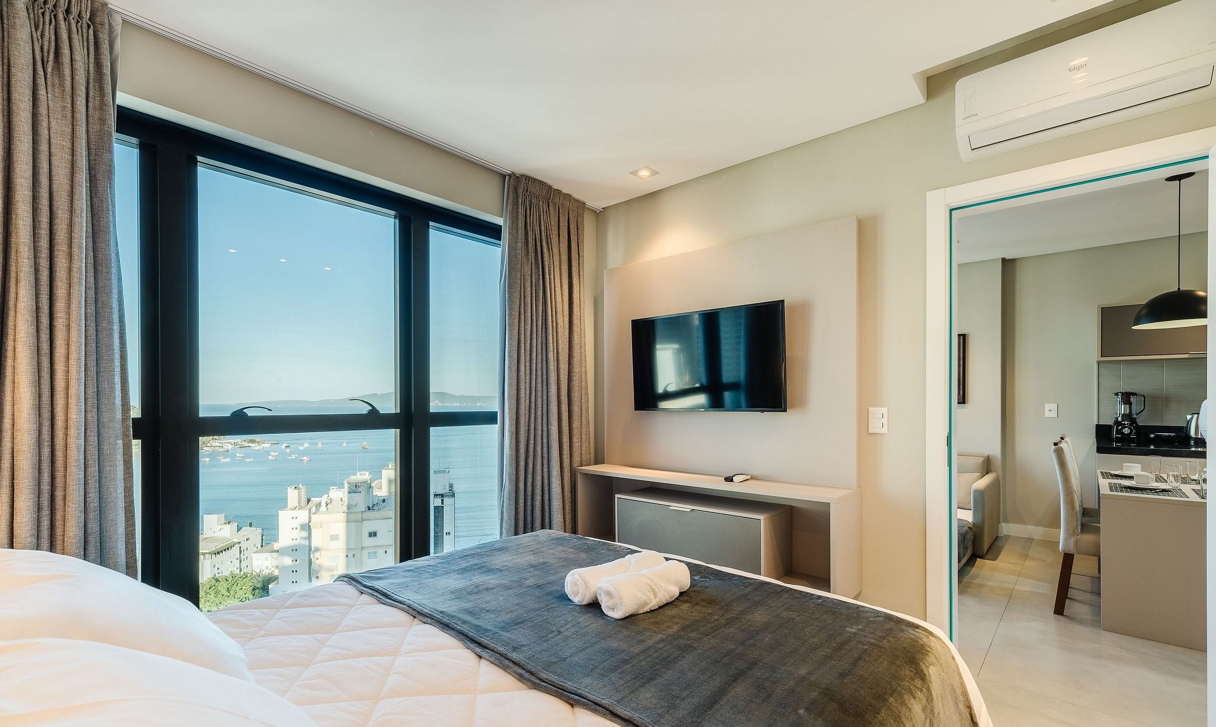 A hotel room with a bed, a TV, a desk, and a view of the city.