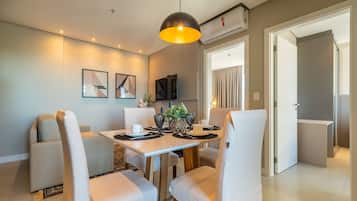Un comedor moderno con una mesa y sillas blancas, una lámpara colgante y un televisor de pantalla plana montado en la pared.