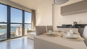 A modern hotel room with a dining area, a large window with a view of the sea and buildings, and a minimalist design. - MHFs Apartamentos com Vista Mar Itapema (Itapema)