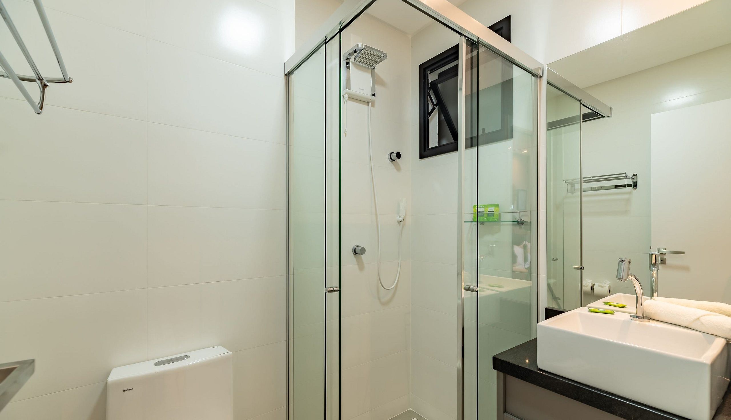 Un baño moderno con ducha envuelta en vidrio, un lavabo blanco con espejo y un inodoro.